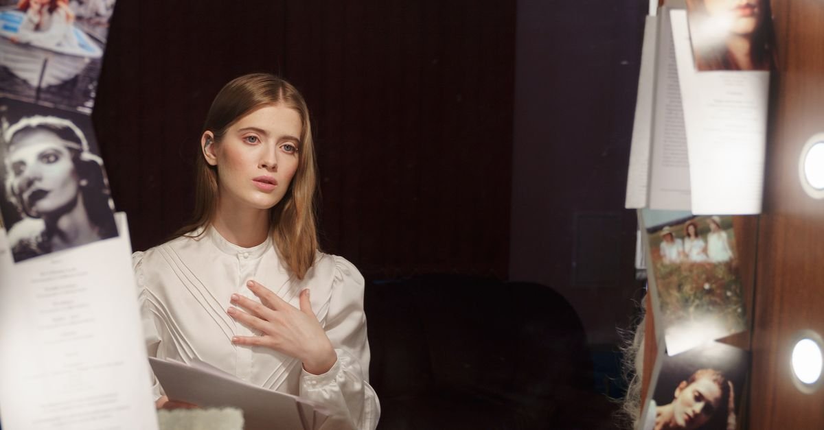 A contemplative actress in a dressing room, reading a script in front of an illuminated mirror.