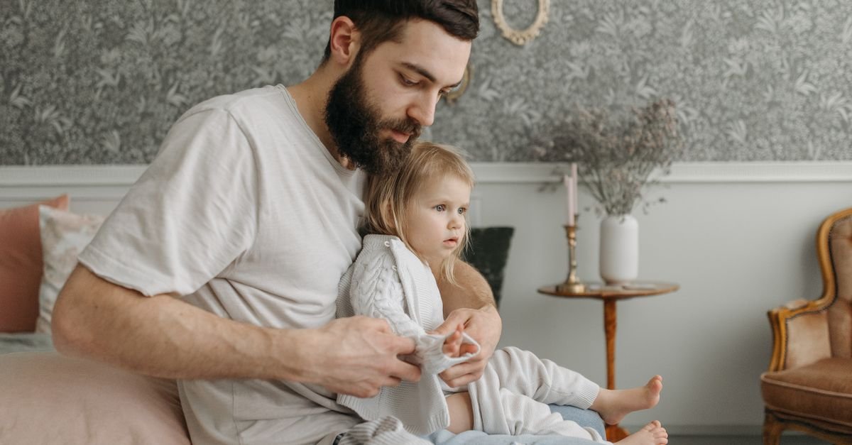 Father helping daughter get dressed in a cozy bedroom environment, highlighting nurturing parenting moments.