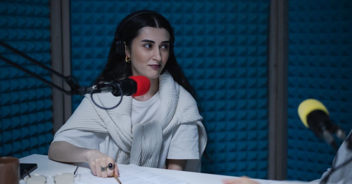 A woman in a podcast studio with microphones and headphones, focused on a discussion.