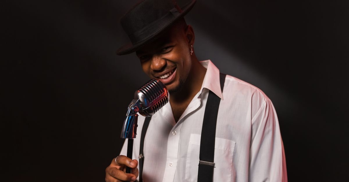 A stylish singer smiling while performing with a vintage microphone.