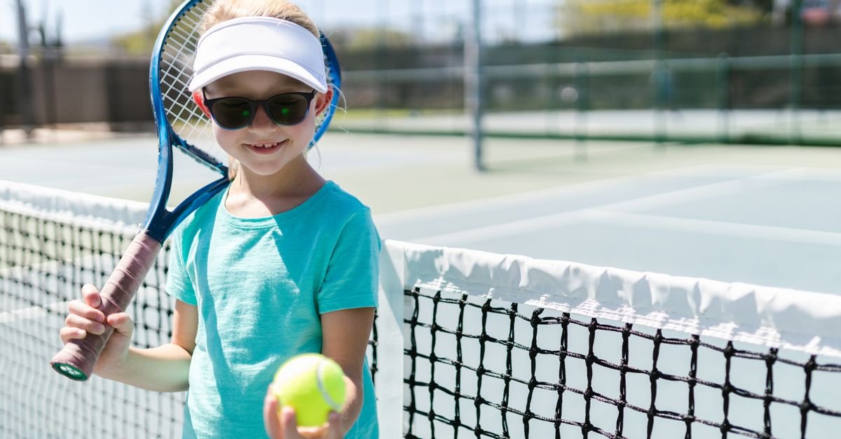 Smiling girl holding tennis racket and ball on a sunny tennis court.