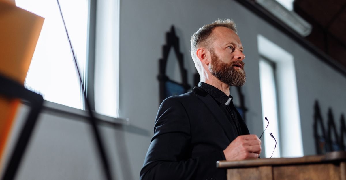 A priest passionately delivers a sermon from a pulpit inside a church.