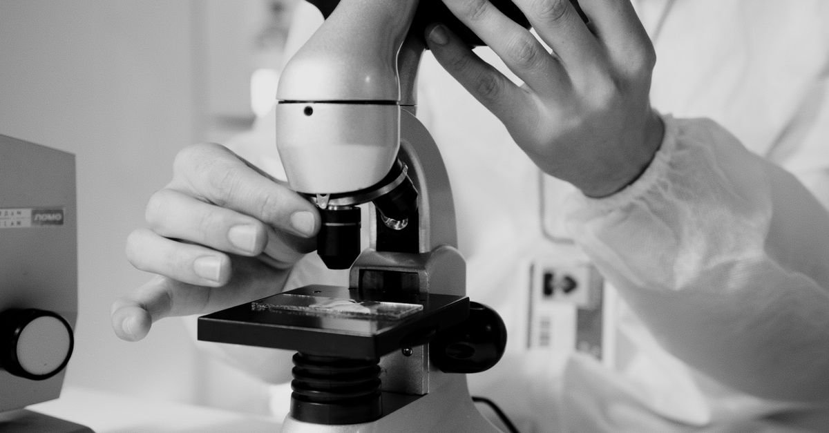 A scientist in a lab coat using a microscope for research in a laboratory setting.