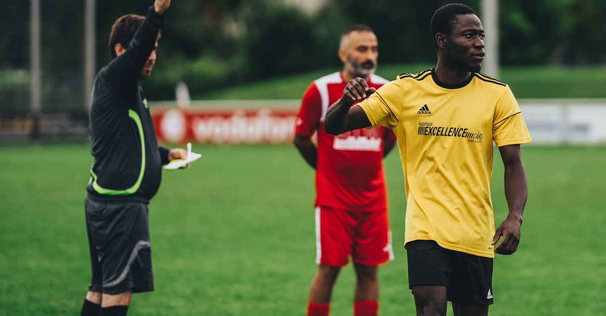 Referee issuing a red card to a soccer player in an outdoor match setting.