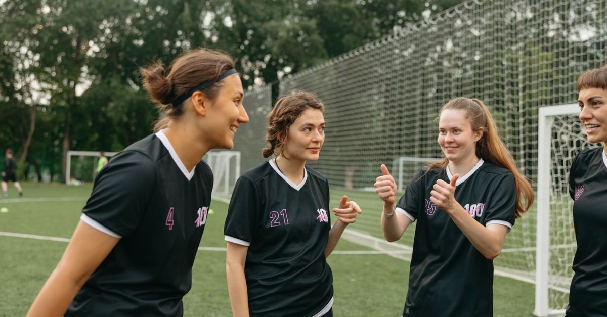 Group of female soccer players in black uniforms bonding outdoors, fostering teamwork.