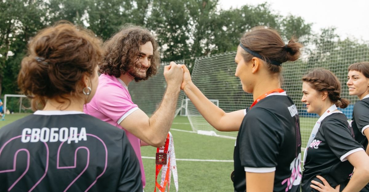 Soccer team celebrating victory on field with coach, exchanging fist bumps and medals.