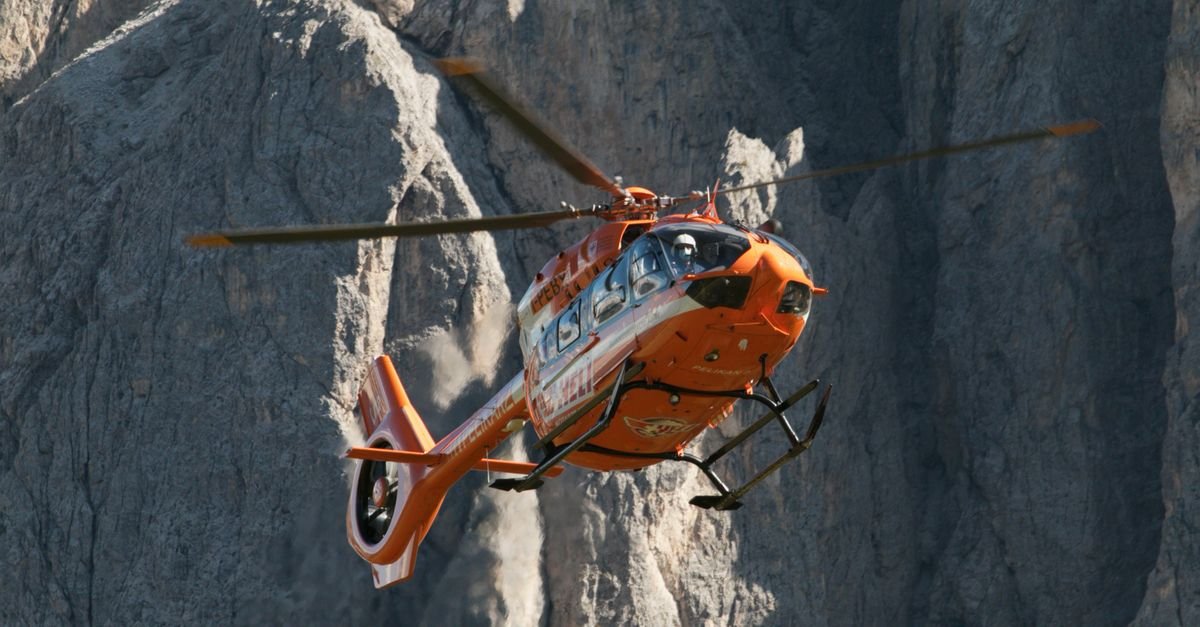 A bright orange rescue helicopter flying amidst the rugged Dolomites mountains.